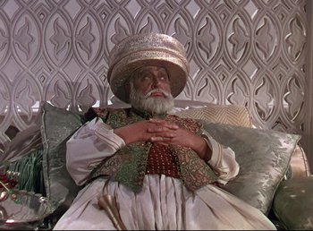 Movie still from “Arabian Nights” (1942), directed by John Rawlins – An old man sitting on a couch wearing a hat; Medium shot, Low angle