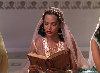 Movie still from “Arabian Nights” (1942), directed by John Rawlins – A woman wearing a headpiece and reading a book; Medium shot, High angle
