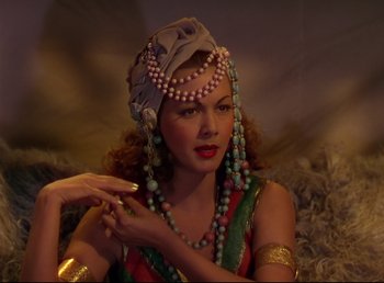 Movie still from “Arabian Nights” (1942), directed by John Rawlins – A woman in a colorful dress and a hat; Close Up shot, Low angle