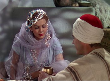 Movie still from “Arabian Nights” (1942), directed by John Rawlins – A woman wearing a veil and a turban is holding a cup; Medium shot, Over the shoulder angle