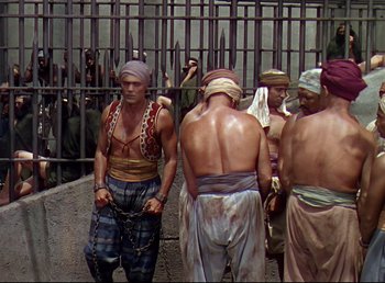 Movie still from “Arabian Nights” (1942), directed by John Rawlins – A group of men standing next to each other in chains; Wide shot, High angle