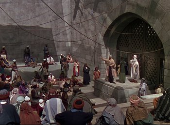 Movie still from “Arabian Nights” (1942), directed by John Rawlins – A group of people sitting on a stage in front of an audience; Extreme Wide shot, High angle