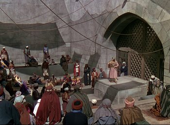 Movie still from “Arabian Nights” (1942), directed by John Rawlins – A group of people sitting on a stage in front of an audience; Extreme Wide shot, High angle