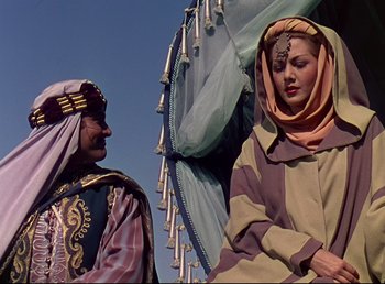 Movie still from “Arabian Nights” (1942), directed by John Rawlins – A woman in a headscarf and a man in a turban stand in front of an umbrella; Medium shot, Low angle