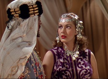 Movie still from “Arabian Nights” (1942), directed by John Rawlins – A woman in a purple dress and a man in a white suit; Medium shot, Over the shoulder angle