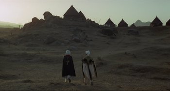 Movie still from “Arabian Nights” (1974), directed by Pier Paolo Pasolini – Two people in traditional clothing walking in the desert; Extreme Wide shot, Low angle