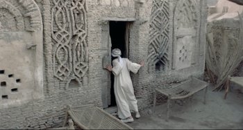 Movie still from “Arabian Nights” (1974), directed by Pier Paolo Pasolini – A man in a white robe standing in front of a door; Wide shot, Over the shoulder angle