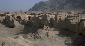 Movie still from “Arabian Nights” (1974), directed by Pier Paolo Pasolini – A man standing on top of a dirt hill near some buildings; Extreme Wide shot, High angle