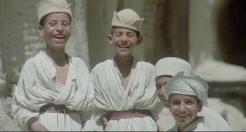 Movie still from “Arabian Nights” (1974), directed by Pier Paolo Pasolini – A group of young men wearing white clothes and white hats; Medium shot, Low angle