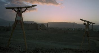 Movie still from “Arabian Nights” (1974), directed by Pier Paolo Pasolini – The sun sets over a desert landscape with a cross; Extreme Wide shot, Low angle