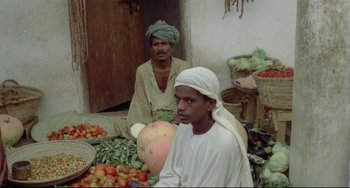 Movie still from “Arabian Nights” (1974), directed by Pier Paolo Pasolini – Two men sitting in front of a pile of fruit; Medium shot, High angle