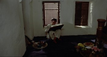 Movie still from “Arabian Nights” (1974), directed by Pier Paolo Pasolini – A man sitting on the ground reading a book; Wide shot, High angle