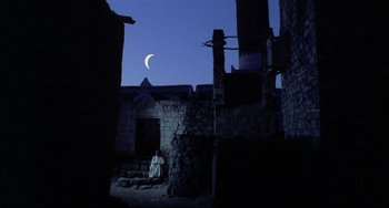 Movie still from “Arabian Nights” (1974), directed by Pier Paolo Pasolini – A person sitting on a stone wall in the dark; Extreme Wide shot, Low angle