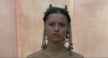 Movie still from “Arabian Nights” (1974), directed by Pier Paolo Pasolini – A young woman wearing a pair of earrings and a head piece; Close Up shot, Low angle