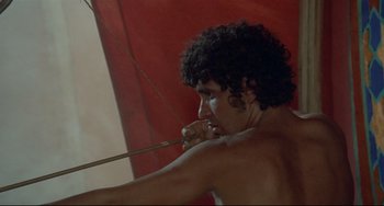 Movie still from “Arabian Nights” (1974), directed by Pier Paolo Pasolini – A man with curly hair is holding a bow and arrow; Medium shot, Over the shoulder angle