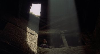 Movie still from “Arabian Nights” (1974), directed by Pier Paolo Pasolini – A man sitting in a cave looking up at the sky; Extreme Wide shot, Low angle