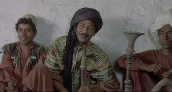 Movie still from “Arabian Nights” (1974), directed by Pier Paolo Pasolini – A man with a turban on sitting on a chair; Medium shot, Low angle