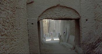 Movie still from “Arabian Nights” (1974), directed by Pier Paolo Pasolini – A group of people walking down a path in an alley way; Extreme Wide shot, High angle