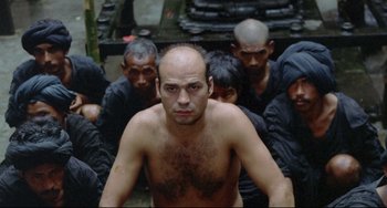 Movie still from “Arabian Nights” (1974), directed by Pier Paolo Pasolini – A man with a bald head is surrounded by a group of men; Medium shot, High angle