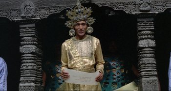 Movie still from “Arabian Nights” (1974), directed by Pier Paolo Pasolini – A man in a gold outfit holding a piece of paper in his hands; Medium shot, Over the shoulder angle
