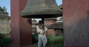 Movie still from “Arabian Nights” (1974), directed by Pier Paolo Pasolini – A man standing under a large bell near a building; Wide shot, Low angle