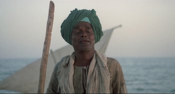 Movie still from “Arabian Nights” (1974), directed by Pier Paolo Pasolini – A man in a turban is meditating in front of a boat; Close Up shot, Low angle