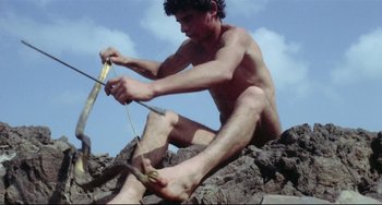 Movie still from “Arabian Nights” (1974), directed by Pier Paolo Pasolini – A man sitting on top of a rock holding a knife; Medium shot, High angle