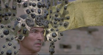 Movie still from “Arabian Nights” (1974), directed by Pier Paolo Pasolini – A man wearing a metal helmet with a lot of metal parts on it; Close Up shot, Low angle