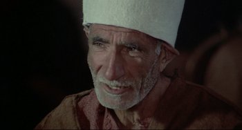 Movie still from “Arabian Nights” (1974), directed by Pier Paolo Pasolini – An old man wearing a white hat looking at the camera; Close Up shot, Over the shoulder angle