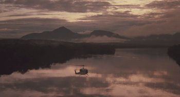 Movie still from “Arachnophobia” (1990), directed by Frank Marshall – A helicopter flying over a body of water at sunset; Extreme Wide shot, High angle