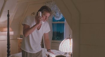 Movie still from “Arachnophobia” (1990), directed by Frank Marshall – A young man talking on a phone while standing in front of a lamp; Medium shot, Low angle