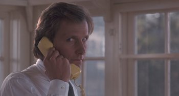 Movie still from “Arachnophobia” (1990), directed by Frank Marshall – A man in a white dress shirt and tie holding a yellow phone to his ear; Close Up shot, Low angle