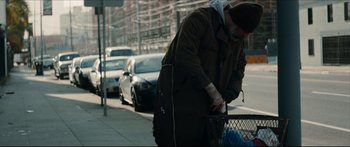 Movie still from “Archenemy” (2020), directed by Adam Egypt Mortimer – A man standing on the side of the street with a basket; Medium shot, Low angle