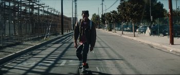 Movie still from “Archenemy” (2020), directed by Adam Egypt Mortimer – A man riding a skateboard down the middle of the street; Wide shot, Low angle