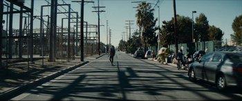 Movie still from “Archenemy” (2020), directed by Adam Egypt Mortimer – A man riding a skateboard down the middle of a street; Extreme Wide shot, Low angle