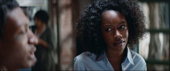 Movie still from “Archenemy” (2020), directed by Adam Egypt Mortimer – A black woman with curly black hair is looking at the camera; Close Up shot, Over the shoulder angle