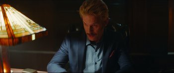 Movie still from “Archenemy” (2020), directed by Adam Egypt Mortimer – A man with blonde hair wearing a blue suit; Close Up shot, Over the shoulder angle