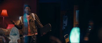 Movie still from “Archenemy” (2020), directed by Adam Egypt Mortimer – A person holding a skateboard in a room; Medium shot, Over the shoulder angle
