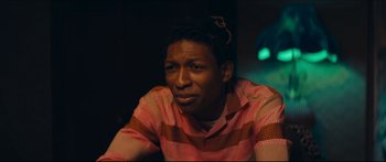 Movie still from “Archenemy” (2020), directed by Adam Egypt Mortimer – A man in a pink and brown striped shirt is looking at the camera; Close Up shot, Over the shoulder angle