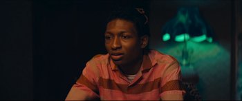 Movie still from “Archenemy” (2020), directed by Adam Egypt Mortimer – A man in a pink and orange shirt is looking at the camera; Close Up shot, Over the shoulder angle