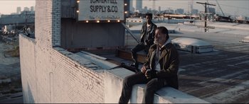Movie still from “Archenemy” (2020), directed by Adam Egypt Mortimer – Two men sitting on the side of a building; Wide shot, Low angle