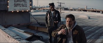 Movie still from “Archenemy” (2020), directed by Adam Egypt Mortimer – Two men standing on a roof with one holding a can of beer; Medium shot, Low angle