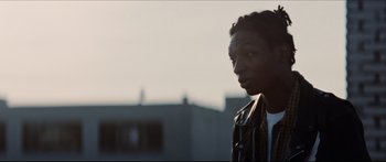 Movie still from “Archenemy” (2020), directed by Adam Egypt Mortimer – A young man standing in front of a building; Close Up shot, Low angle