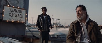 Movie still from “Archenemy” (2020), directed by Adam Egypt Mortimer – A man standing on top of a building in front of a city; Medium shot, Low angle