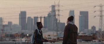 Movie still from “Archenemy” (2020), directed by Adam Egypt Mortimer – Two people are talking in front of a city skyline; Wide shot, Over the shoulder angle