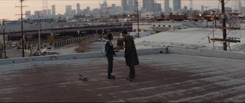 Movie still from “Archenemy” (2020), directed by Adam Egypt Mortimer – Two skateboarders are standing on the roof of a parking lot; Wide shot, Over the shoulder angle