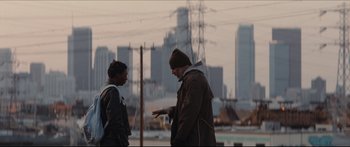 Movie still from “Archenemy” (2020), directed by Adam Egypt Mortimer – Two men are talking in front of a city skyline; Medium shot, Over the shoulder angle