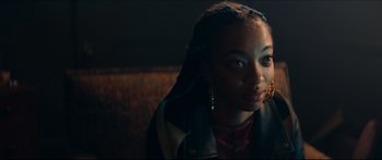 Movie still from “Archenemy” (2020), directed by Adam Egypt Mortimer – A young woman with braids is looking into the camera; Close Up shot, Over the shoulder angle