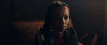 Movie still from “Archenemy” (2020), directed by Adam Egypt Mortimer – A young woman with braids wearing a leather jacket; Close Up shot, Over the shoulder angle