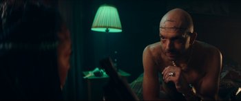 Movie still from “Archenemy” (2020), directed by Adam Egypt Mortimer – A man with a tattoo on his face looking at himself in the mirror; Medium shot, Over the shoulder angle